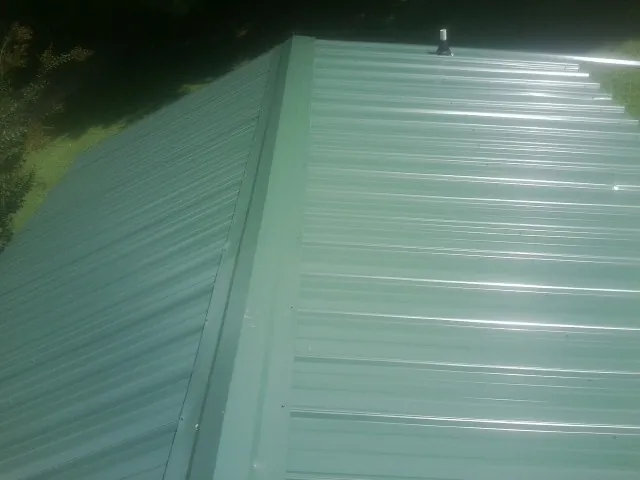 New green metal panels meeting at the ridge of a roof — Flat Roof Repair work by our crew in Haverhill