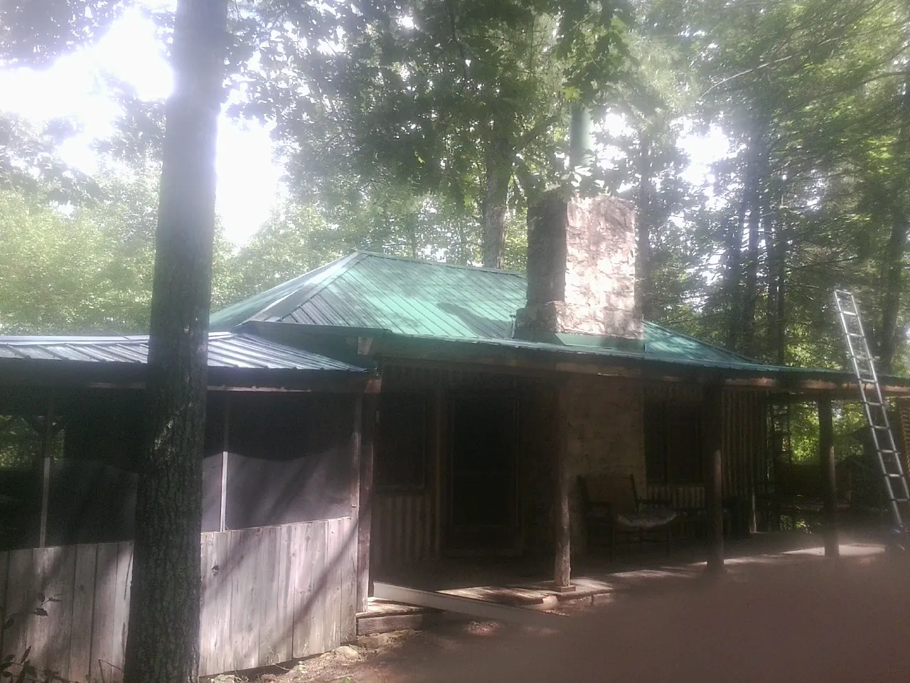 Green metal roof and stone chimney above a log cabin porch in Haverhill