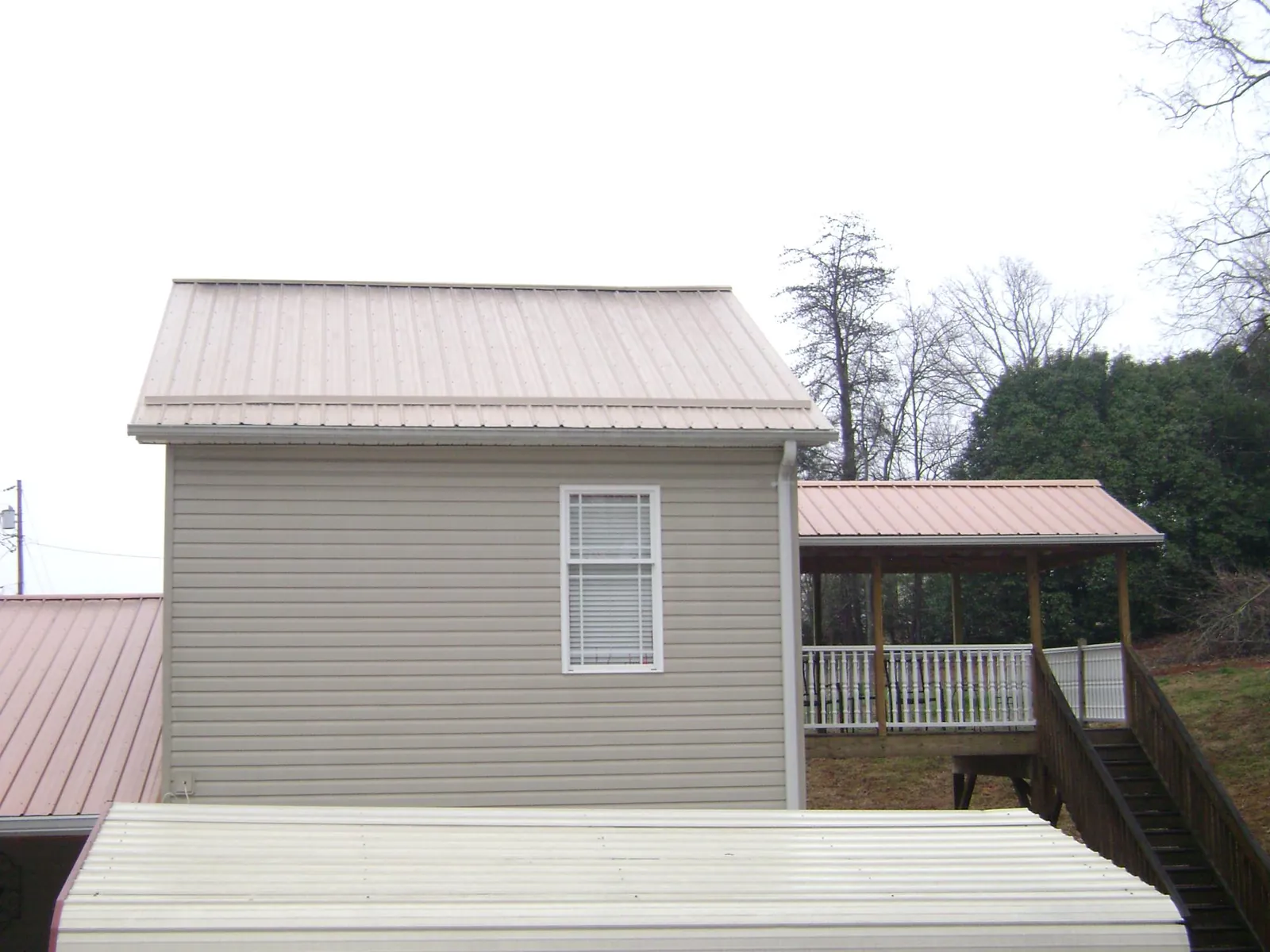 Tan metal roofs on a two story addition and attached porch, from a Roof Replacement job in Haverhill